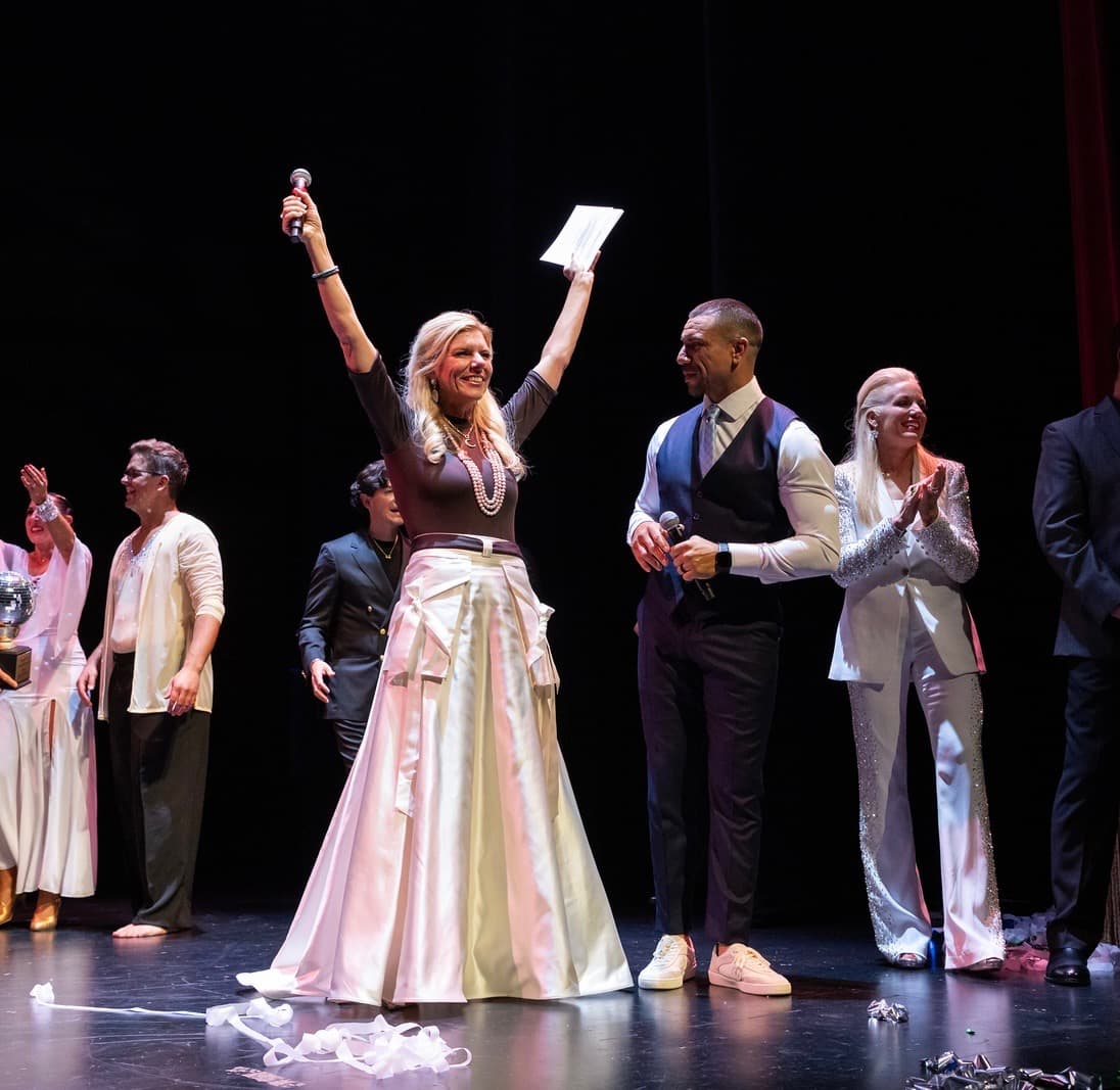 Molly Grantham celebrating on stage at a charity auction, arms raised